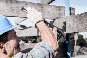 Male worker repairing a wood fence with a hammer - Big Florida Fencing