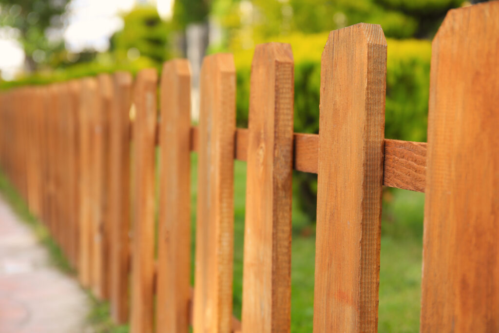 A close-up view of small wooden fence near green bush outdoors - Big Florida Fencing