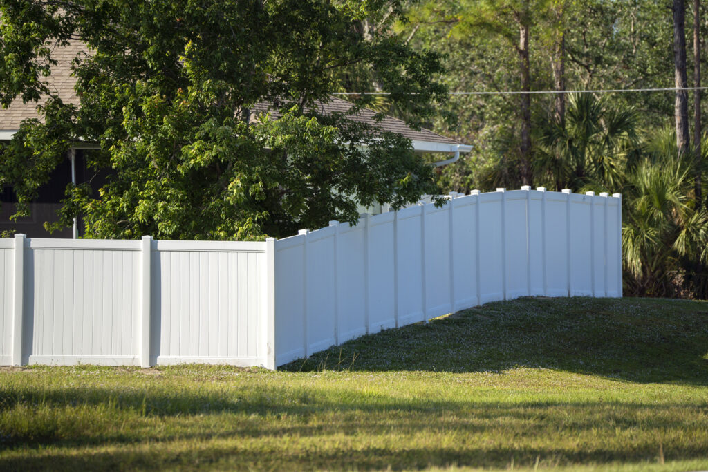 White vinyl picket fence on green lawn surrounding property - Big Florida Fencing